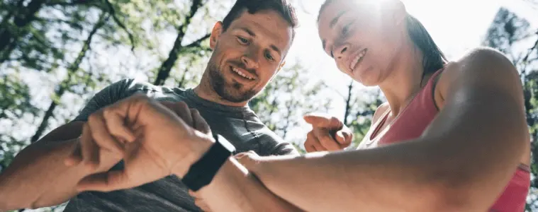 Couple outdoors looking at their smartwatches