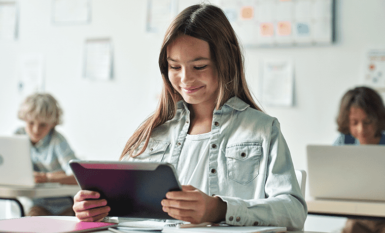 A smiling schoolgirl completes a reading task on her tablet computer in the classroom