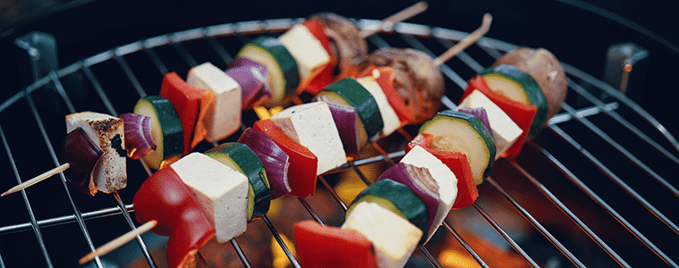 Closeup of vegetable and tofu skewers being grilled on an outdoor barbecue