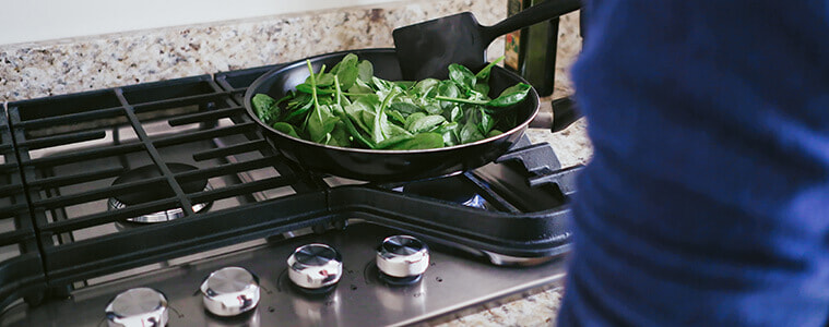 Closeup of a woman sauting spinach on a cooktop