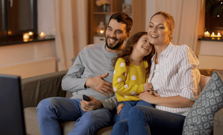 A family sitting on the couch watching TV together 