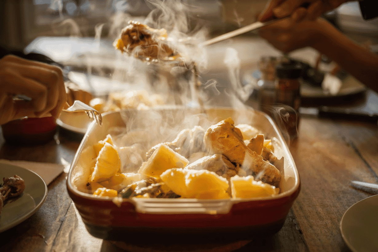 Closeup of a family sitting at the dinner table with steam rising from a dish of roast chicken and vegetables   