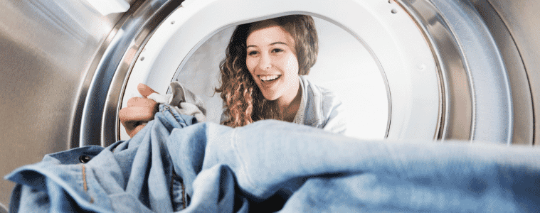 Seen from inside a dryer a woman reaches into the cavity to remove a pair of jeans 