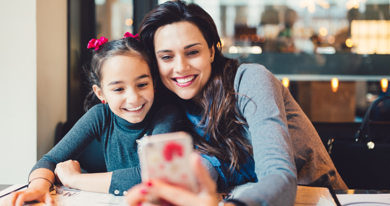 Mother and daughter take selfie on smartphone at cafe. 