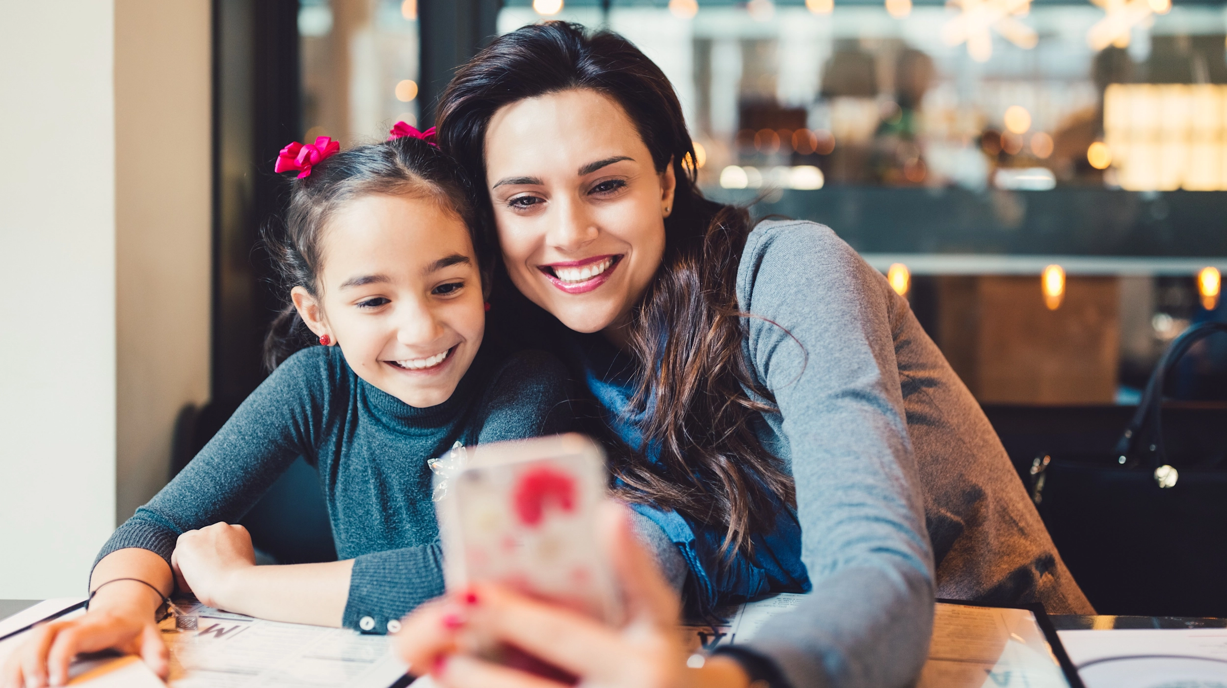 Mother and daughter take selfie on smartphone at cafe.