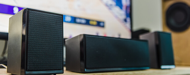 Home theatre speakers lined up at the base of a big screen TV 