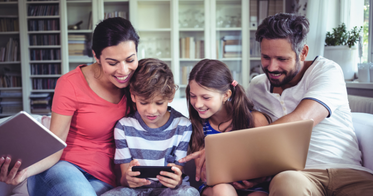 Young family on the couch at home with laptop, tablet and phone.