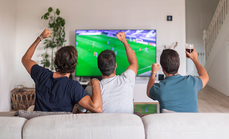 Three friends watching a soccer game raising their arms in the air to cheer on their team