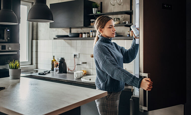 Woman removes a can of soft drink from the fridge in her highend apartment kitchen
