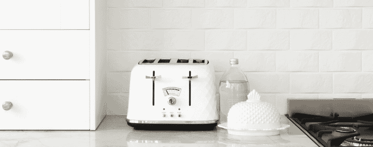 A kettle sits on a bench in front of a white tiled splashback
