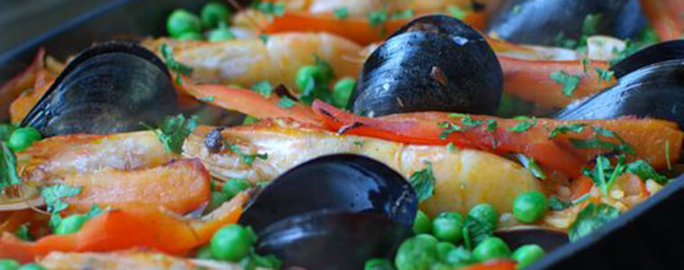 Mussels prawns and seafood in a black bowl on a bbq grill with green peas