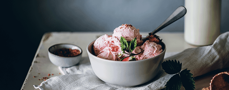 Scoops of delicious homemade strawberry ice cream in a white bowl on a white table with a white linen cloth
