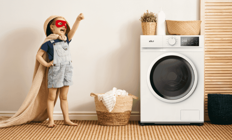 A child wears a superhero mask and uses a clean towel as a cape He stands in a superhero pose next to a Solt washing machine