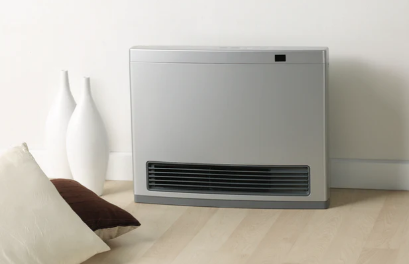 Silver freestanding gas heater on a timber floor beside a wall with decorative vases