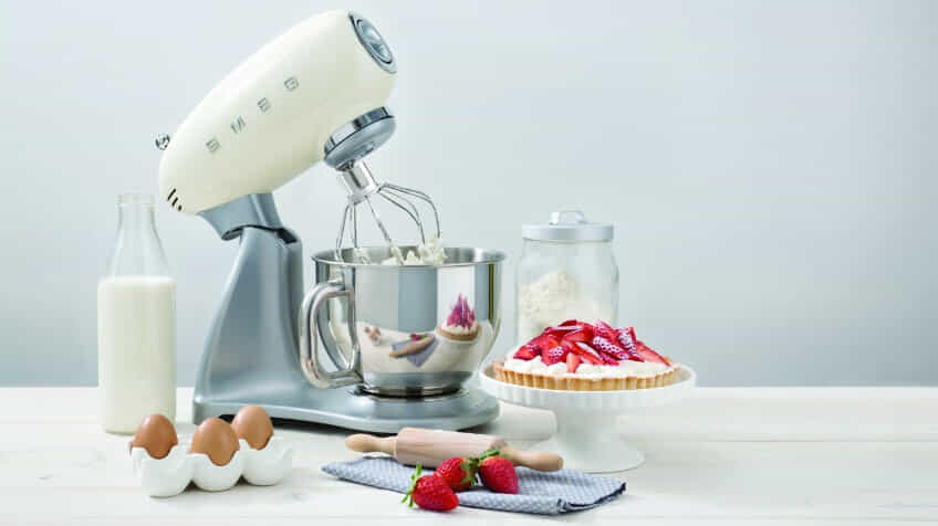 A cream coloured Smeg stand mixer mixes cream for a strawberry pie