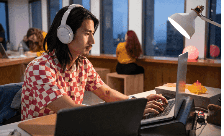 Man happily working on his laptop at a desk whilst using his over ear Bose Noise Cancelling Headphones