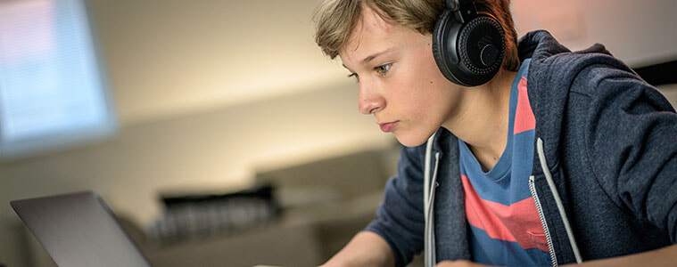 Boy with headphones plays a video game on his laptop at home