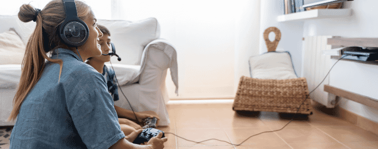 Teenagers sit on the floor and play video games on a console connected to the smart TV in their living room