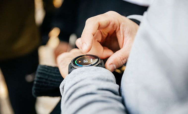 Closeup of a man in a grey tracksuit checking stats on the screen of his smartwatch