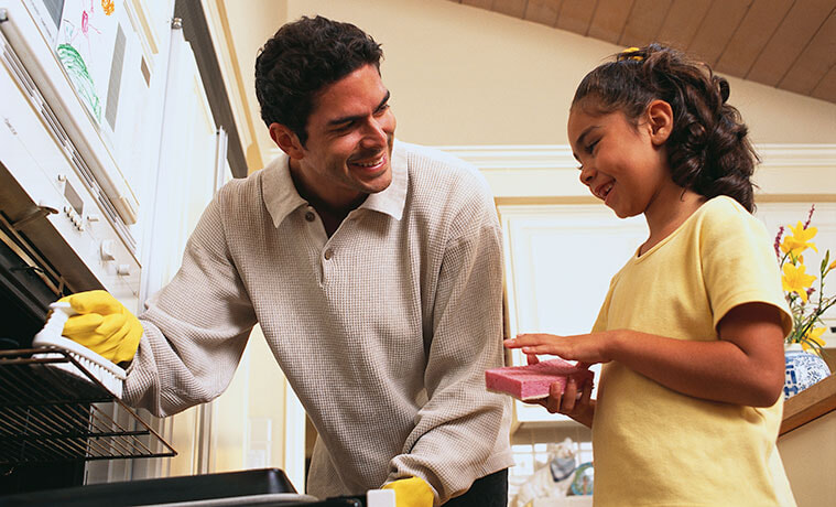 A father cleaning the oven with his daughter 
