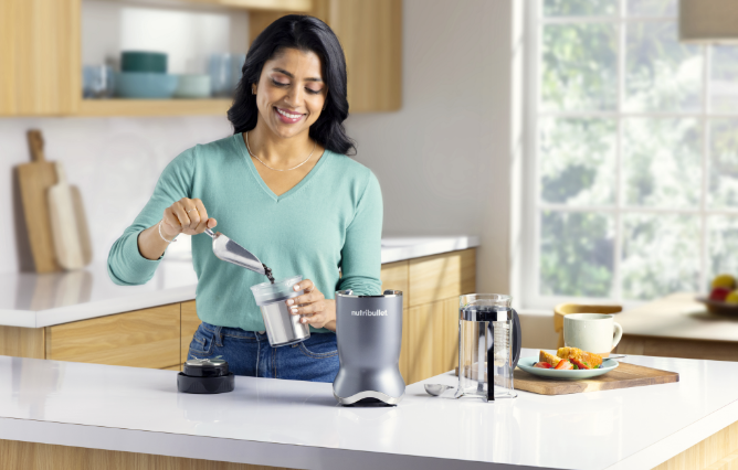 Woman happily pouring coffee beans into her Nutribullet blender in kitchen. 
