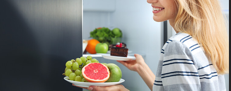 Woman taking plates with fruits and cake from a smart fridge in her kitchen 