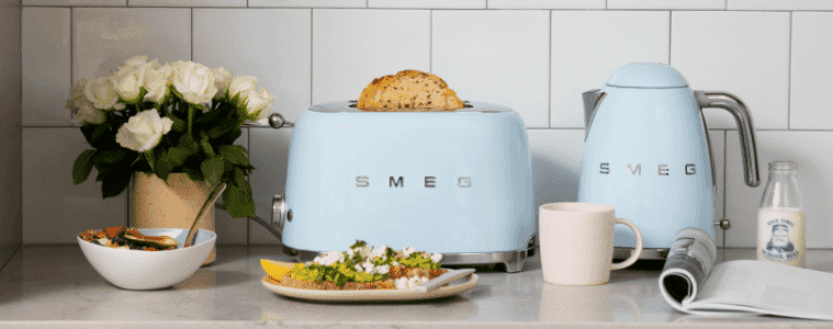 Smeg retro toaster and kettle in sky blue on a white benchtop with an assortment of food around them