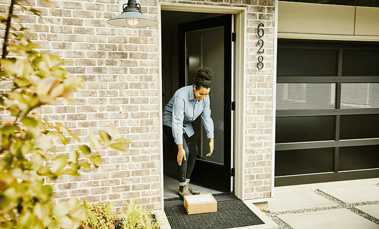 Smiling woman picks up a package from the front porch of her inner city home