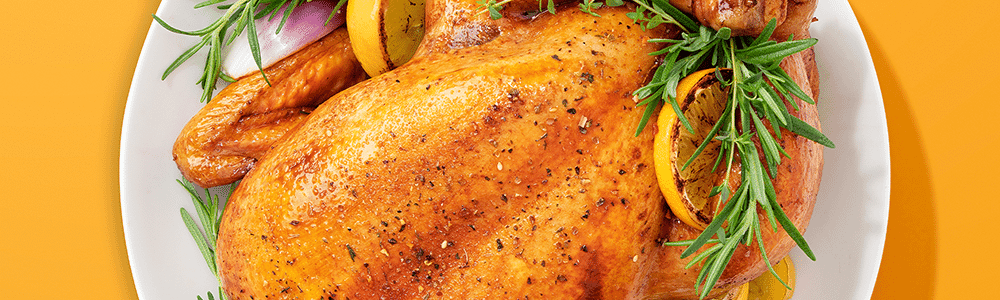 Golden roast chicken on a white plate with caramelised lemon slices herbs and red onion on an orange background Image courtesy of Nutribullet