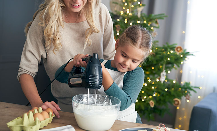 A mother and young daughter use a hand mixer to make cake batter for Christmas baking
