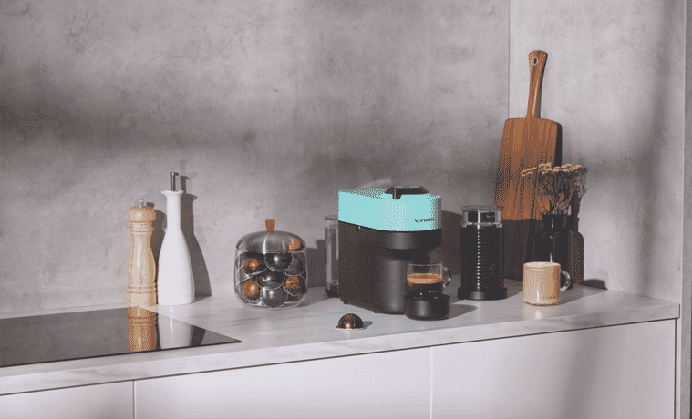 The Nespresso Nespresso Vertuo Pop Bundle in Aqua Mint sits on a grey benchtop in a modern grey kitchen