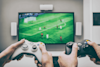 Two sets of hands on video game controllers with a new 4K screen in the background