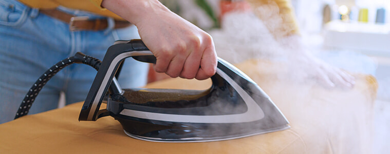 Closeup shot of a man using an iron and ironing board to press the creases from a yellow shirt