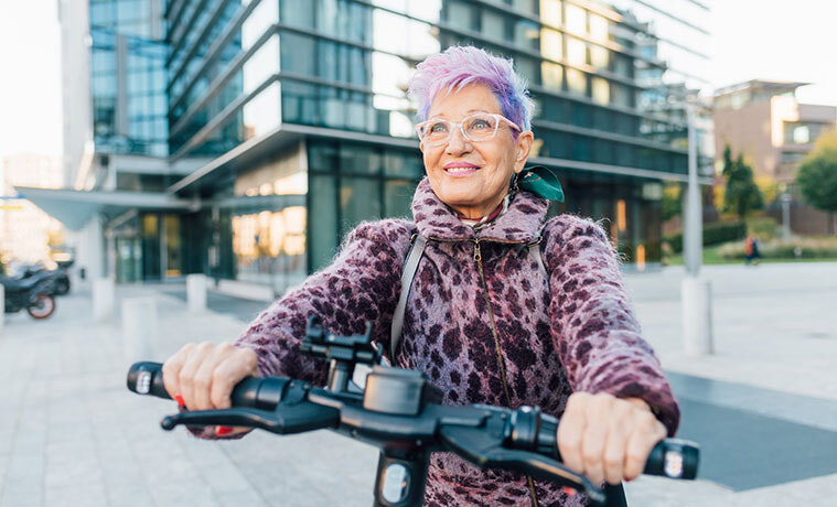 A fashionable older woman smiles while riding an escooter in an inner city location 