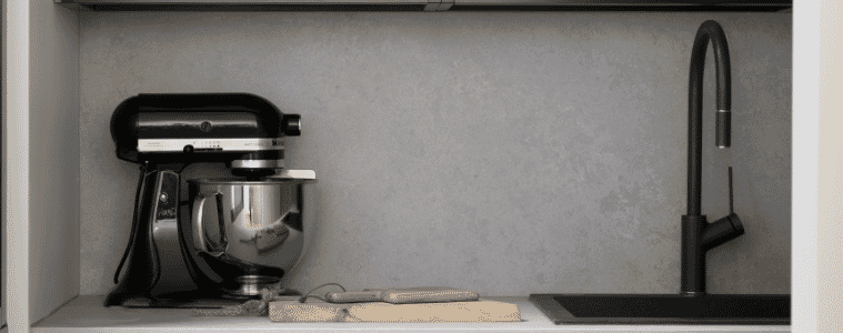 Open shelves with pantry items and a Kitchenaid stand mixer on the bench next to a black sink and tap 