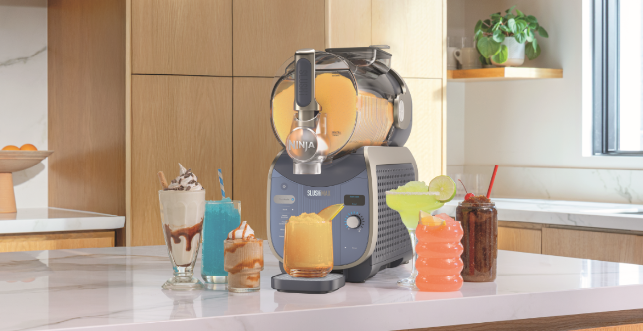 Lifestyle image of a Ninja Slushi Max Smart Frozen Drink Maker Cyberspace on a kitchen bench surrounded by frozen drinks.