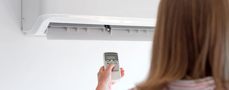 A woman aims a remote control at her wallmounted air conditioner turning it on to cool