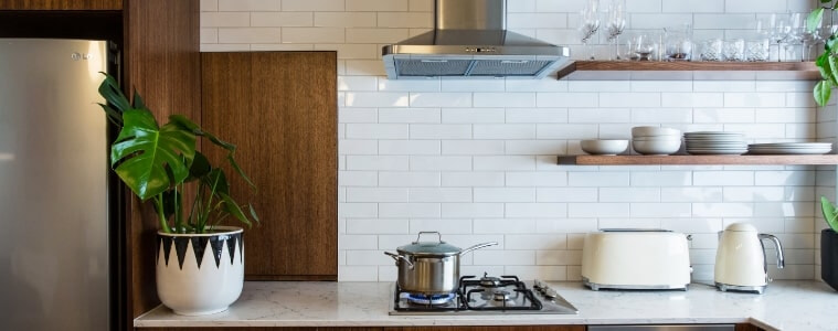 A chrome canopy rangehood in a white and warm timber kitchen