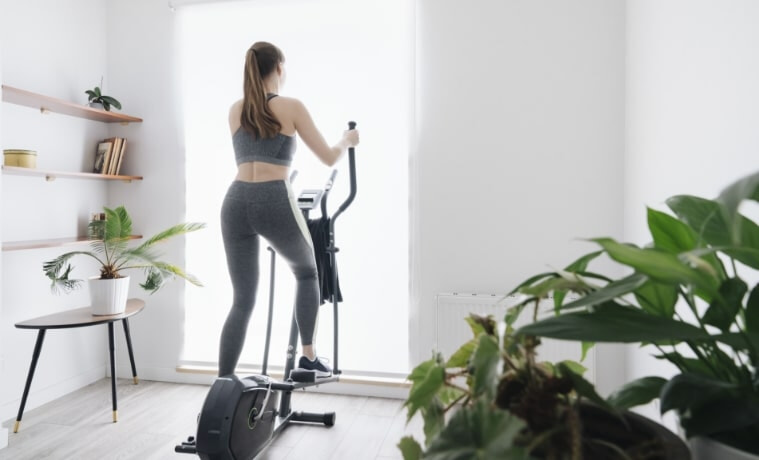 A woman performs a workout on an elliptical trainer at home