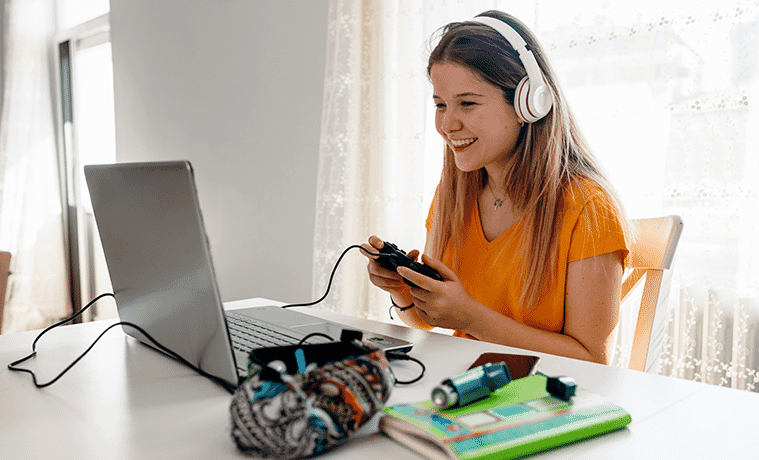 Female uni student with headphones and remote control enjoys a gaming break on a laptop