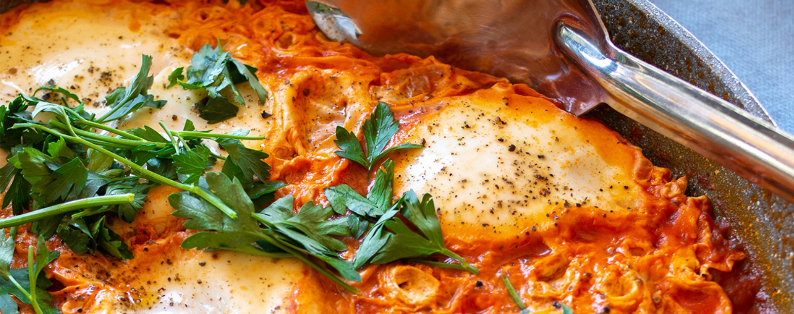Shakshuka in a frying pan, topped with fresh parsley and cracked black pepper.
