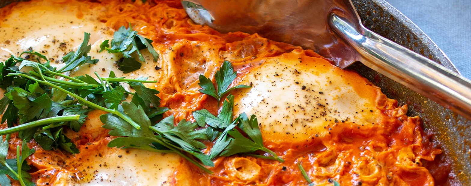 Shakshuka in a frying pan, topped with fresh parsley and cracked black pepper.