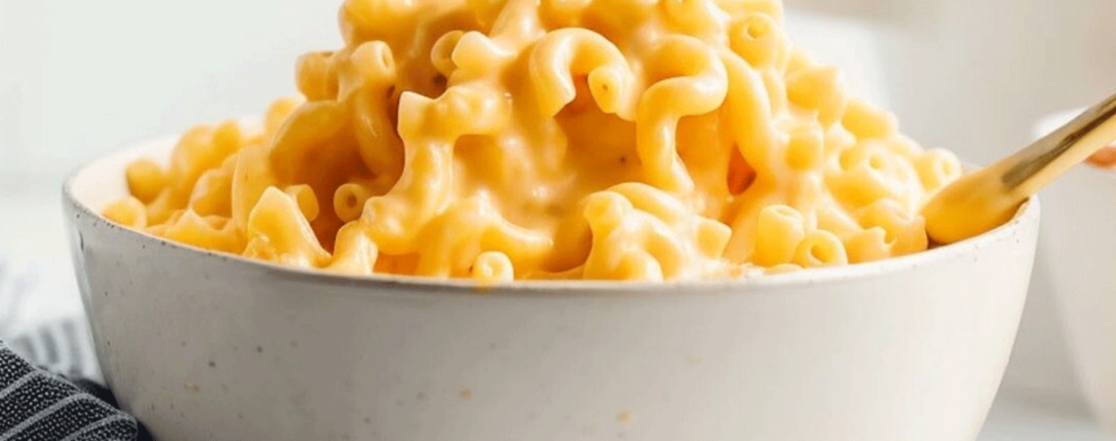 Bowl of creamy macaroni and cheese with a gold spoon.