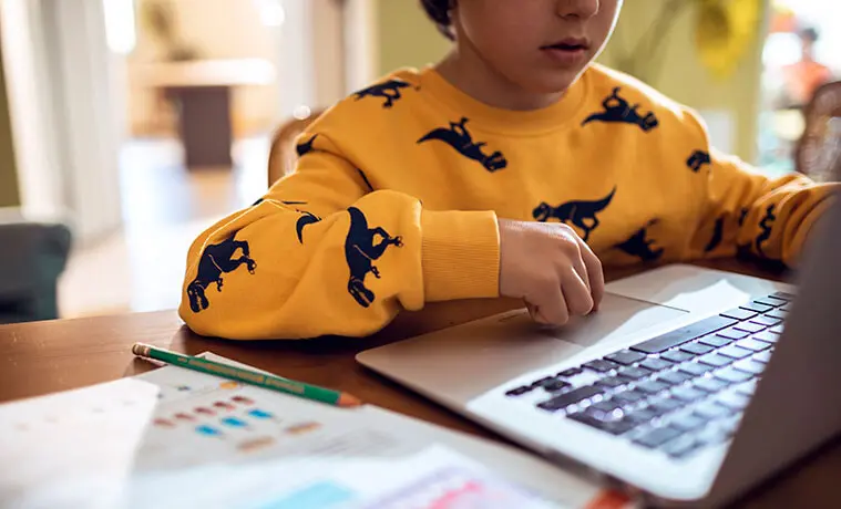 A young boy uses his laptop for homework at the kitchen table