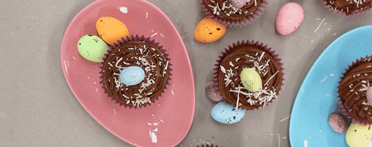 Chocolate cupcakes on pink and blue coloured plates with bright chocolate eggs and desiccated coconut sprinkled on top Image courtesy of Sunbeam