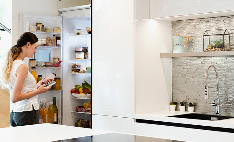 A sideview shot of a woman choosing what healthy snack to get out of her smart fridge