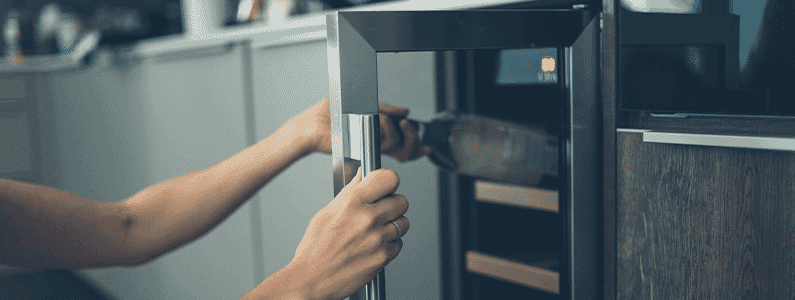 Woman opening her wine fridge in the kitchen to put away a bottle of wine