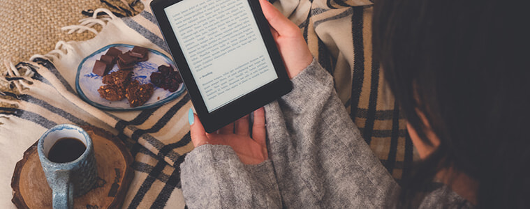 Woman reading a book on her ereader while wrapped in a warm blanket 