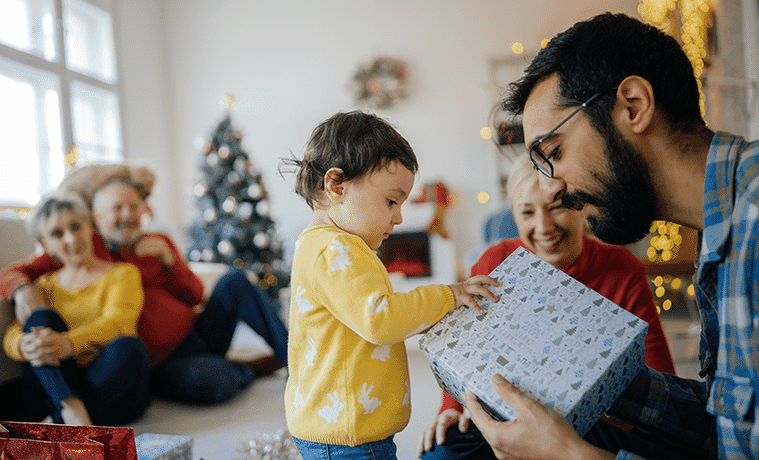 A toddler reaches for a Christmas gift that his father is holding