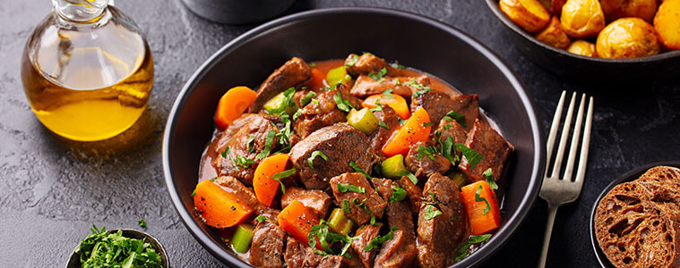 Beef bourguignon in white casserole dish with ladle